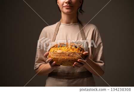 Baker holding artisan fruit and nut bread loaf with golden crust and seeds in warm soft studio lighting Baker holding artisan fruit and nut bread loaf with golden crust and seeds in warm soft studio lighting 134238308