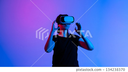 Woman adjusting VR headset while preparing for virtual experience under vibrant blue and pink neon lights Woman adjusting VR headset while preparing for virtual experience under vibrant blue and pink neon lights 134238370