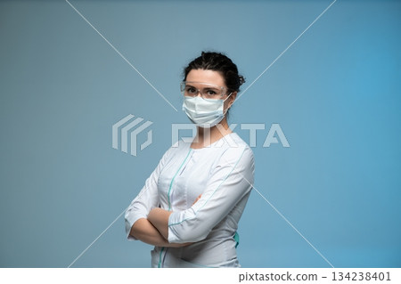 Female doctor in medical mask and protective glasses posing confidently in uniform Female doctor in medical mask and protective glasses posing confidently in uniform 134238401