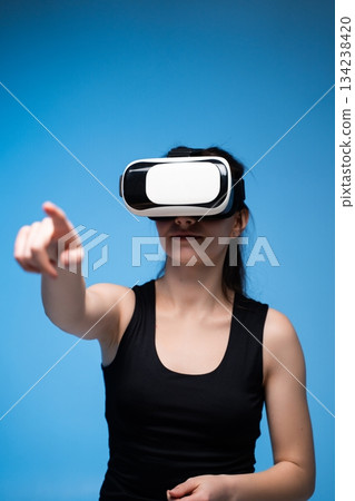 Woman wearing VR headset pointing forward while interacting with immersive futuristic digital environment 134238420
