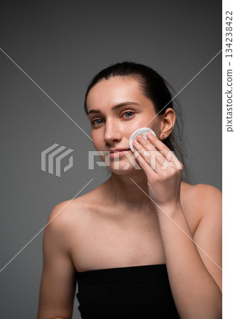 Close-up portrait of woman cleansing facial skin with cotton pad during daily beauty skincare routine Close-up portrait of woman cleansing facial skin with cotton pad during daily beauty skincare routine 134238422