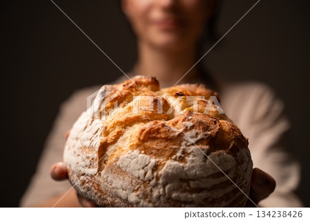 Fresh rustic artisan bread loaf held forward by baker in warm soft light showcasing crisp crust and flour texture 134238426