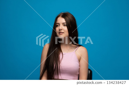Calm young woman looking aside with soft neutral facial expression against clean bright blue studio background Calm young woman looking aside with soft neutral facial expression against clean bright blue studio background 134238427