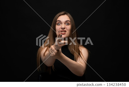 Angry young woman pointing forward with intense aggressive facial expression in dark studio portrait 134238450