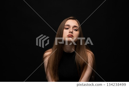 Moody young woman posing with tilted head in low-key studio portrait on black background with soft shadows 134238499