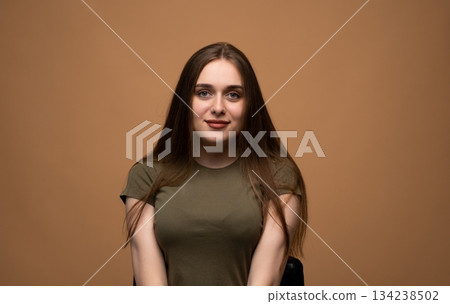 Calm young woman posing for neutral studio portrait on brown background with natural expression and soft light 134238502