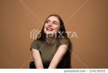 Smiling young woman looking up with joyful expression on brown background, positive human emotion portrait 134238503