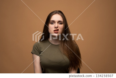 Playful young woman making silly twisted face expression in studio against warm brown background portrait 134238507