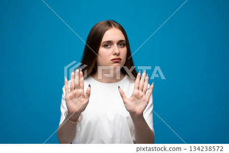 Woman showing both hands in defensive gesture on blue background, stop sign expression portrait Woman showing both hands in defensive gesture on blue background, stop sign expression portrait 134238572