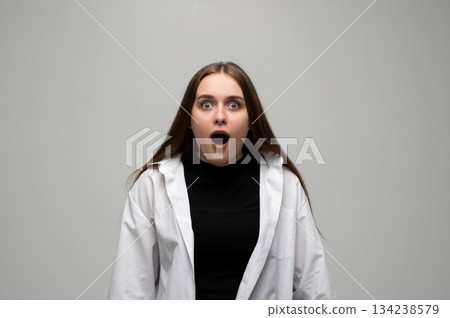 Young woman looking shocked with wide eyes and open mouth in studio portrait on gray background 134238579