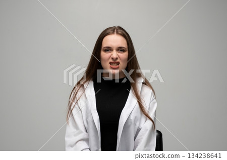 Young woman snarling and showing teeth with tense emotional expression in bright studio setting Young woman snarling and showing teeth with tense emotional expression in bright studio setting 134238641