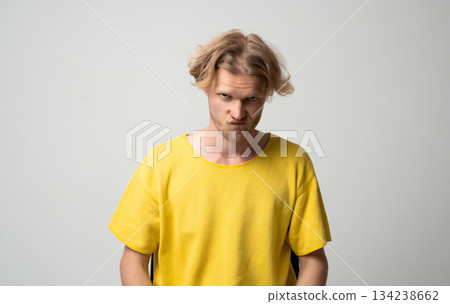 Serious young man in yellow shirt pressing his lips together with intense expression in studio portrait Serious young man in yellow shirt pressing his lips together with intense expression in studio portrait 134238662