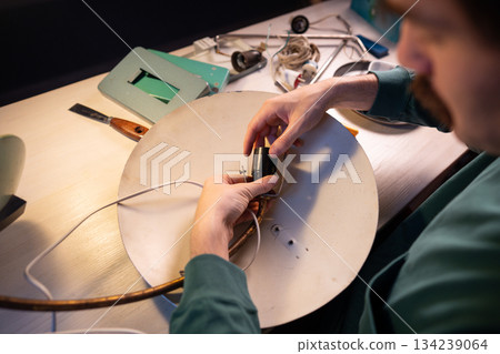 Handyman repairing old vintage electric lamp, disassembling parts of light bulb socket from holder. 134239064