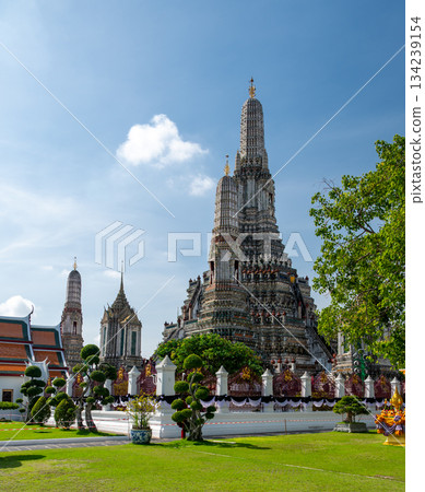 Detailed view of the ornate towers of Wat Arun in Bangkok, Thailand, showcasing rich ceramic floral patterns, sculpted figures, and intricate decorations under bright daylight. 134239154