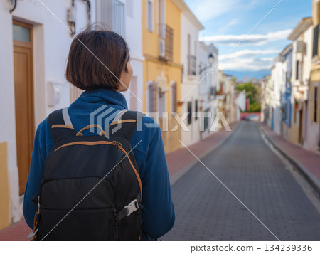 Young woman strolling through charming narrow streets of Denia, Alicante province, Spain, surrounded by historic Mediterranean architecture , enjoying peaceful atmosphere and cultural ambiance. Young woman strolling through charming narrow streets of Denia, Alicante province, Spain, surrounded by historic Mediterranean architecture , enjoying peaceful atmosphere and cultural ambiance. 134239336