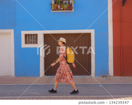 Woman in dress strolls through colorful streets of Spanish coastal town of La Vila Joiosa or Villajoyosa. sunny winter atmosphere highlights charm of Mediterranean architecture and quiet seaside life Woman in dress strolls through colorful streets of Spanish coastal town of La Vila Joiosa or Villajoyosa. sunny winter atmosphere highlights charm of Mediterranean architecture and quiet seaside life 134239347
