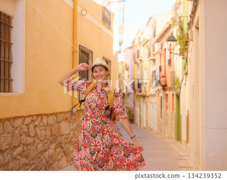 Woman in dress strolls through colorful streets of Spanish coastal town of La Vila Joiosa or Villajoyosa. sunny winter atmosphere highlights charm of Mediterranean architecture and quiet seaside life 134239352