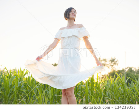 Beautiful woman in white dress standing in summer field during golden sunset in Croatia, warm sunlight, romantic evening mood, natural countryside atmosphere, soft wind and peaceful scene Beautiful woman in white dress standing in summer field during golden sunset in Croatia, warm sunlight, romantic evening mood, natural countryside atmosphere, soft wind and peaceful scene 134239355