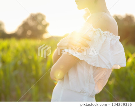 Beautiful woman in white dress standing in summer field during golden sunset in Croatia, warm sunlight, romantic evening mood, natural countryside atmosphere, soft wind and peaceful scene Beautiful woman in white dress standing in summer field during golden sunset in Croatia, warm sunlight, romantic evening mood, natural countryside atmosphere, soft wind and peaceful scene 134239356