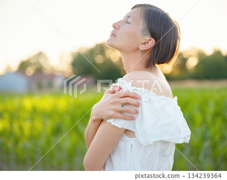 Beautiful woman in white dress standing in summer field during golden sunset in Croatia, warm sunlight, romantic evening mood, natural countryside atmosphere, soft wind and peaceful scene Beautiful woman in white dress standing in summer field during golden sunset in Croatia, warm sunlight, romantic evening mood, natural countryside atmosphere, soft wind and peaceful scene 134239364