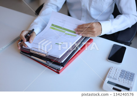 Businessman working in office reading, signing stack of documents. Businessman working in office reading, signing stack of documents. 134240576