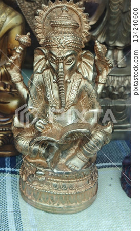 Golden Ganesha statue with detailed ornaments and symbolic attributes displayed on a decorative surface. The image represents Hindu spirituality, wisdom, prosperity and traditional religious art Golden Ganesha statue with detailed ornaments and symbolic attributes displayed on a decorative surface. The image represents Hindu spirituality, wisdom, prosperity and traditional religious art 134240600
