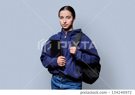Portrait of beautiful female teenage student with backpack, laptop on gray background 134240972