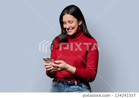 Beautiful smiling woman using smartphone, on grey studio background Beautiful smiling woman using smartphone, on grey studio background 134241357