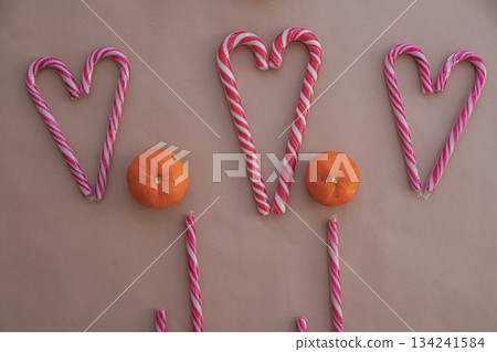 Three Heart-Shaped Candy Canes with Tangerines on Beige Background 134241584