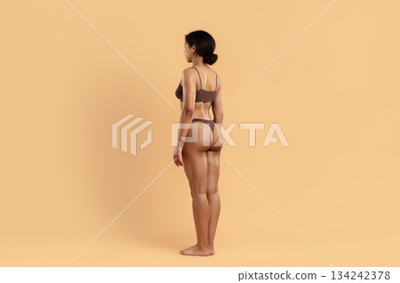 Side profile of young black woman in underwear standing on beige background Side profile of young black woman in underwear standing on beige background 134242378