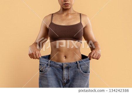 Young black woman showing oversized jeans after weightloss Young black woman showing oversized jeans after weightloss 134242386