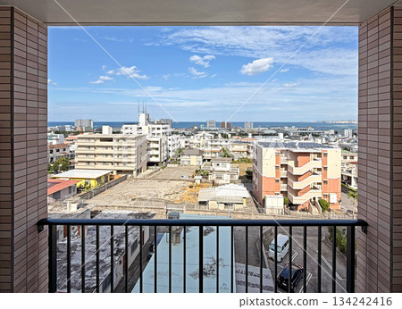A panoramic vista of a sunlit urban landscape featuring diverse architecture, distant ocean, and a bright blue sky dotted with clouds 134242416