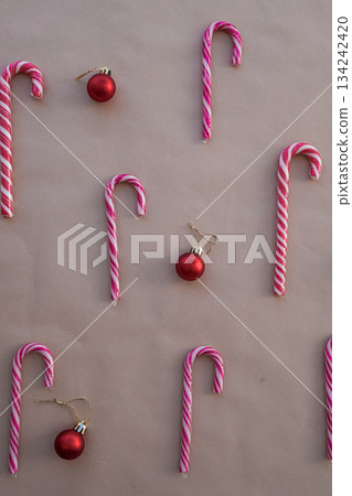 Vertical Flat Lay of Red and White Candy Canes with Glossy Christmas Ornaments on Beige Background Vertical Flat Lay of Red and White Candy Canes with Glossy Christmas Ornaments on Beige Background 134242420