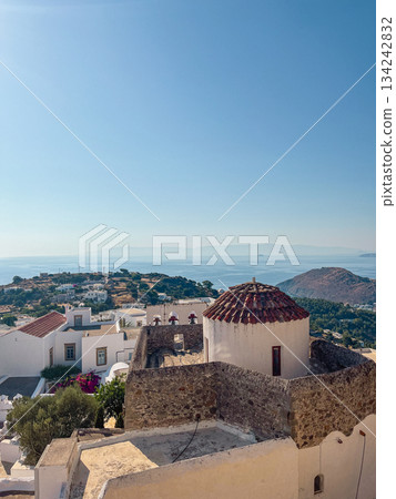 Patmos chora village showcasing classic cycladic architecture with white buildings, stone walls, and a domed chapel, offering a scenic view of the blue sea and surrounding landscape Patmos chora village showcasing classic cycladic architecture with white buildings, stone walls, and a domed chapel, offering a scenic view of the blue sea and surrounding landscape 134242832