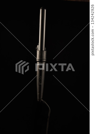 hair curling iron rests on a dark surface showcasing its design and structure. The setting highlights the styling tools used for hair. It is ready for use in a hair care routine. hair curling iron rests on a dark surface showcasing its design and structure. The setting highlights the styling tools used for hair. It is ready for use in a hair care routine. 134242926