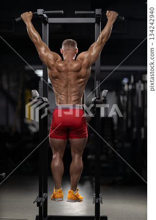 athlete works on strength by doing pull ups in a gym. This scene captures the dedication and focus required during an evening workout routine. athlete works on strength by doing pull ups in a gym. This scene captures the dedication and focus required during an evening workout routine. 134242940