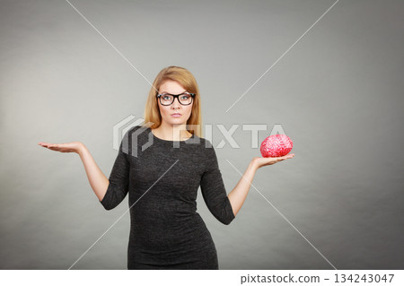 Woman in eyeglasses being confused holding brain 134243047