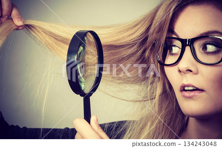 Woman holding magnifying glass looking at hair 134243048