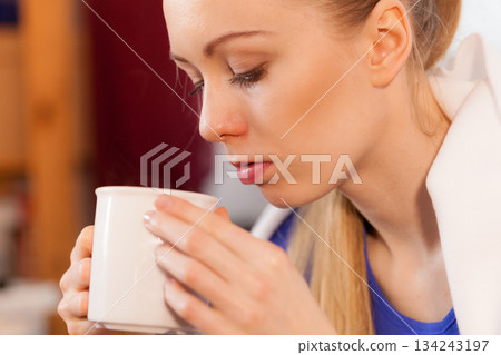 Woman lying on sofa under blanket drinking tea 134243197