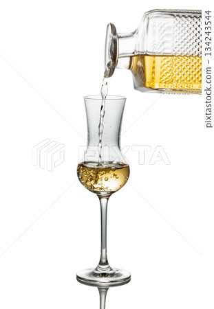 Gold liquor pouring into a glass on a white background. Gold liquor pouring into a glass on a white background. 134243544
