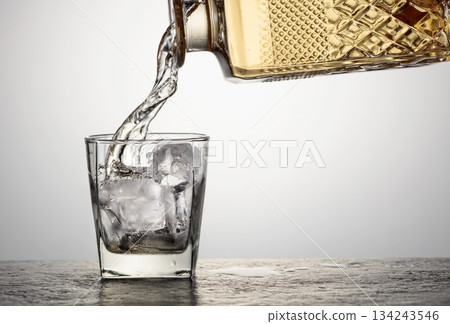 Whiskey is poured from a decanter into a glass with ice. Whiskey is poured from a decanter into a glass with ice. 134243546
