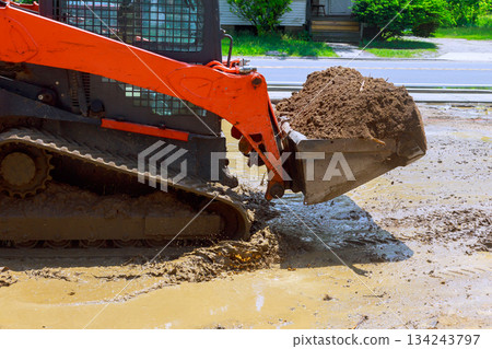 Construction equipment moves dirt mud at worksite street in residential area Construction equipment moves dirt mud at worksite street in residential area 134243797