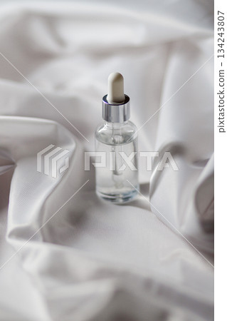 Glass dropper bottle with clear liquid on white satin fabric Glass dropper bottle with clear liquid on white satin fabric 134243807