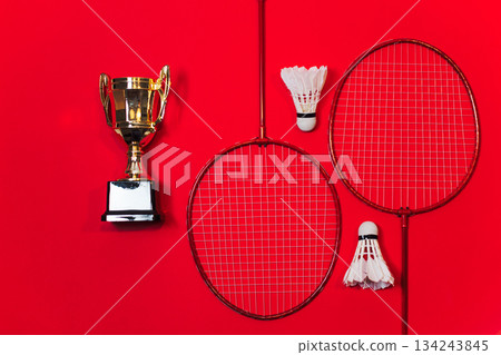 Golden Trophy Stands Beside Two Badminton Rackets And Two White Shuttlecocks Against Red Background 134243845