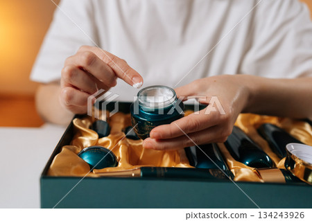 Female hands applying face cream from luxury cosmetic product set, using finger to take nourishing moisturizing cream from stylish jar, symbolizing beauty and self-care routine. Female hands applying face cream from luxury cosmetic product set, using finger to take nourishing moisturizing cream from stylish jar, symbolizing beauty and self-care routine. 134243926