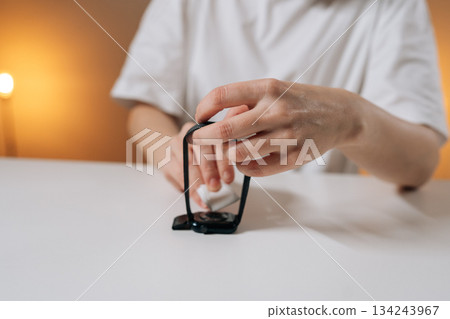 Person taking care of wearable technology device, cleaning smartwatch sensor with soft cloth, ensuring hygiene and proper maintenance of modern personal electronic gadget for daily use. 134243967