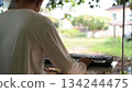 Daytime Outdoor Music White Shirted Musician At Light Colored Table With Keyboard, Green Background Soft Light 134244475
