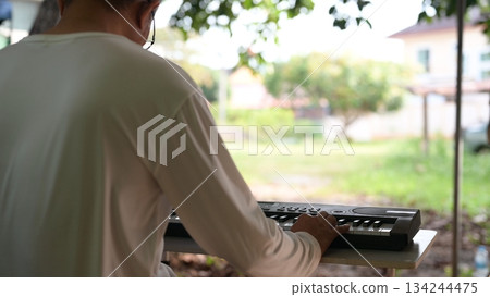 Daytime Outdoor Music White Shirted Musician At Light Colored Table With Keyboard, Green Background Soft Light 134244475