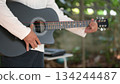 Black Acoustic Guitar Playing Green Scene, White Shirt, Dark Shorts, Hand On Sound hole, Natural Light 134244487