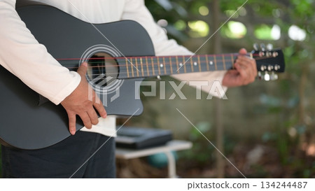Black Acoustic Guitar Playing Green Scene, White Shirt, Dark Shorts, Hand On Sound hole, Natural Light 134244487